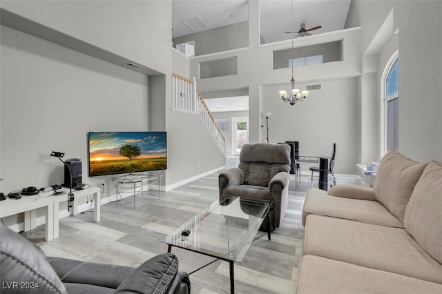 living room with ceiling fan with notable chandelier, light hardwood / wood-style floors, and a towering ceiling