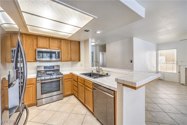 kitchen featuring sink, kitchen peninsula, a textured ceiling, appliances with stainless steel finishes, and tile countertops