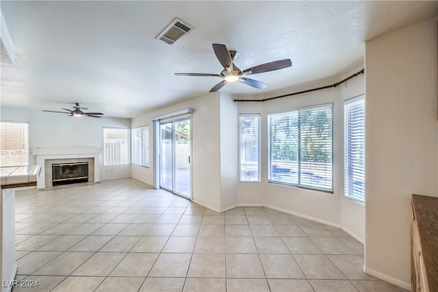 unfurnished living room with ceiling fan, light tile patterned floors, and a textured ceiling