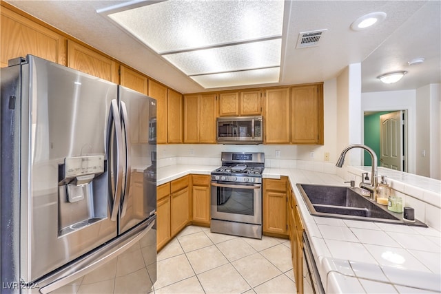 kitchen featuring stainless steel appliances, kitchen peninsula, tile countertops, and sink