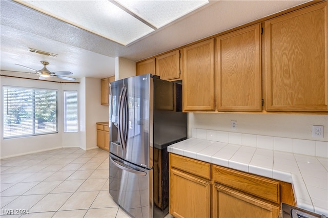 kitchen with light tile patterned floors, tile countertops, a textured ceiling, ceiling fan, and stainless steel fridge with ice dispenser