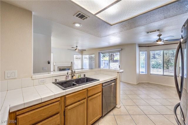 kitchen featuring ceiling fan, tile counters, sink, and stainless steel dishwasher