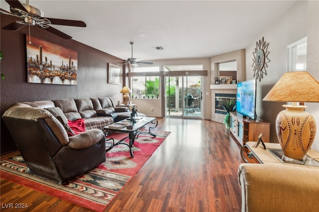 living room featuring wood-type flooring, ceiling fan, and a tile fireplace