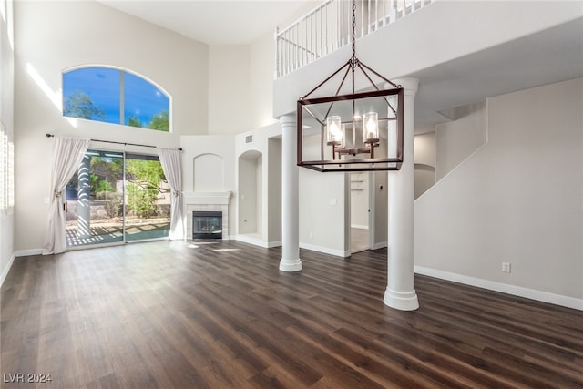 unfurnished living room with dark hardwood / wood-style floors, ornate columns, a towering ceiling, and a notable chandelier