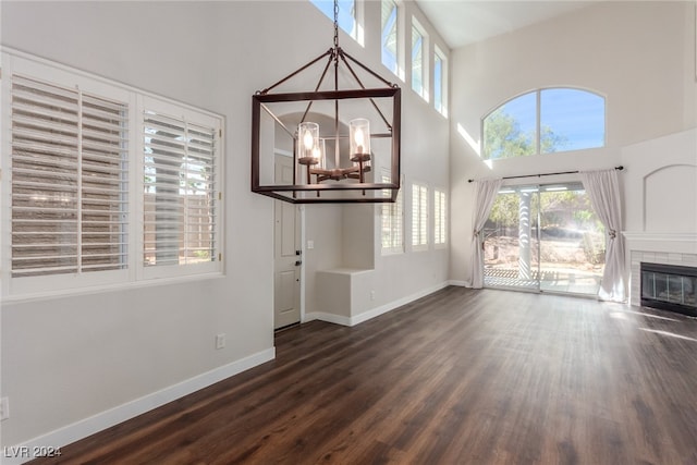 unfurnished living room featuring a towering ceiling, an inviting chandelier, plenty of natural light, and dark hardwood / wood-style floors