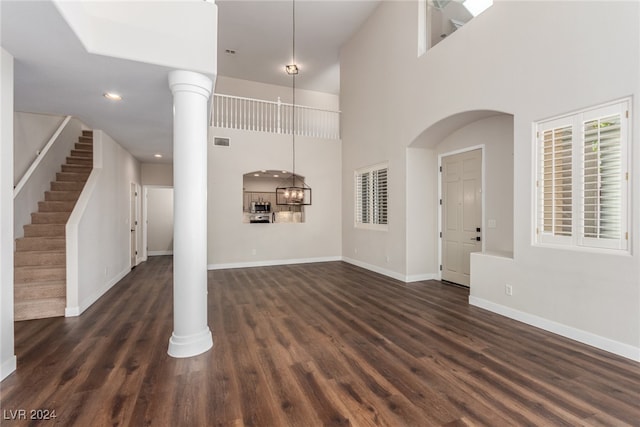 unfurnished living room with a notable chandelier, decorative columns, a towering ceiling, and dark hardwood / wood-style flooring