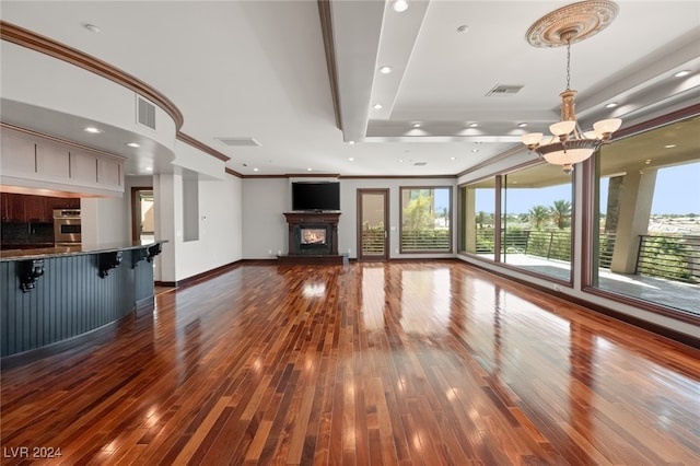 unfurnished living room featuring a notable chandelier, a raised ceiling, hardwood / wood-style flooring, and ornamental molding