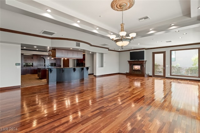 unfurnished living room with wood-type flooring, a chandelier, sink, and crown molding