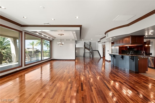 unfurnished living room featuring crown molding, hardwood / wood-style floors, sink, and a notable chandelier