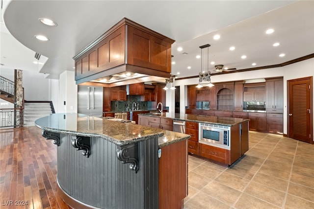 kitchen with hanging light fixtures, dark stone countertops, stainless steel appliances, crown molding, and a large island