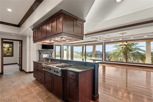 kitchen with dark stone counters, light hardwood / wood-style floors, stainless steel gas cooktop, dark brown cabinetry, and ornamental molding