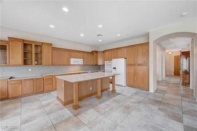 kitchen featuring white appliances, light tile patterned floors, a kitchen island with sink, and a breakfast bar area