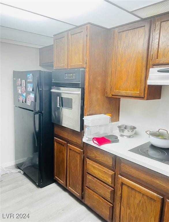 kitchen featuring black refrigerator, cooktop, exhaust hood, light hardwood / wood-style floors, and oven