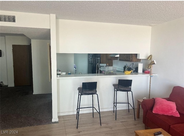 kitchen featuring a breakfast bar area, kitchen peninsula, light hardwood / wood-style flooring, and ventilation hood