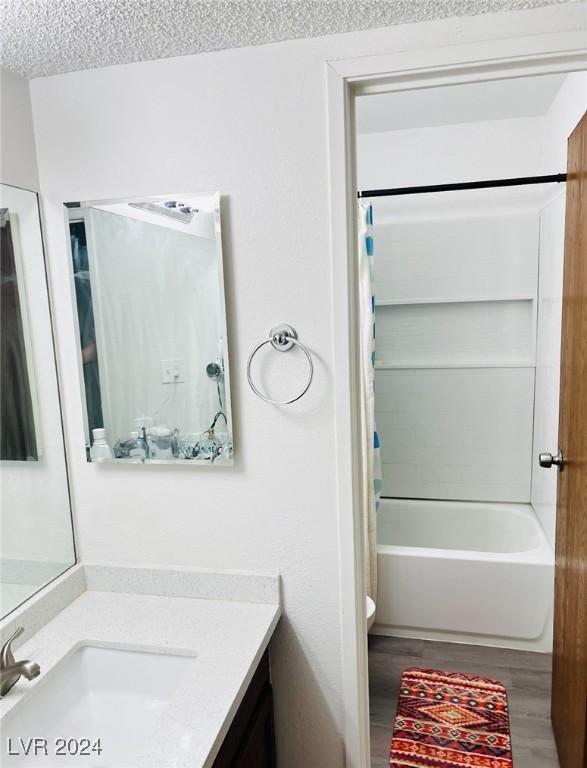 full bathroom with vanity, hardwood / wood-style flooring, toilet, shower / bath combo with shower curtain, and a textured ceiling