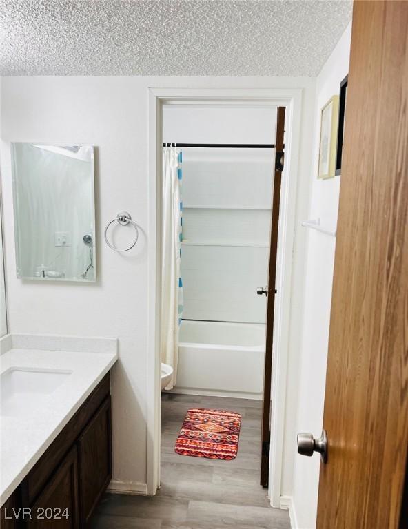 bathroom with a textured ceiling, vanity, hardwood / wood-style flooring, and shower / tub combo with curtain