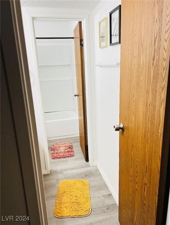 hallway with light wood-type flooring and a textured ceiling