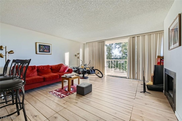 living room with a wall of windows, light wood-type flooring, and a textured ceiling