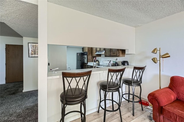 kitchen featuring kitchen peninsula, black fridge, a breakfast bar, and a textured ceiling