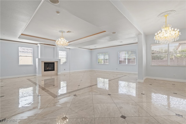 unfurnished living room featuring a chandelier, a healthy amount of sunlight, a raised ceiling, and a tile fireplace