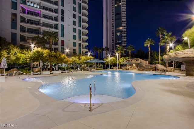 pool at night featuring a patio