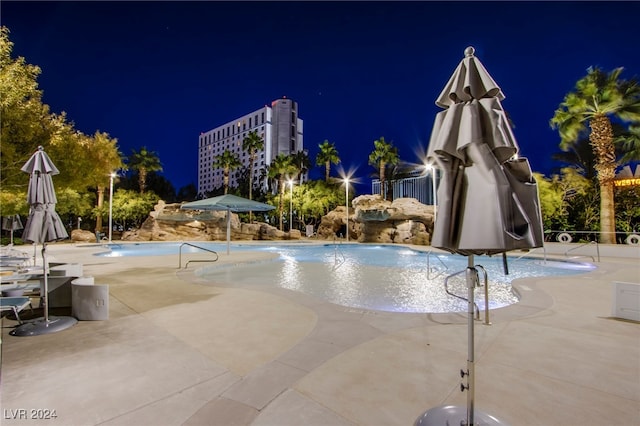 pool at night featuring pool water feature and a patio area