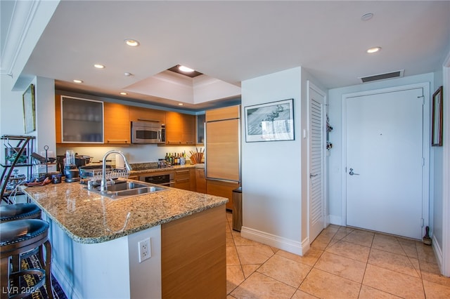 kitchen with a raised ceiling, light tile patterned floors, sink, kitchen peninsula, and a kitchen breakfast bar