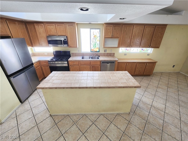 kitchen with light tile patterned floors, tile counters, stainless steel appliances, and sink