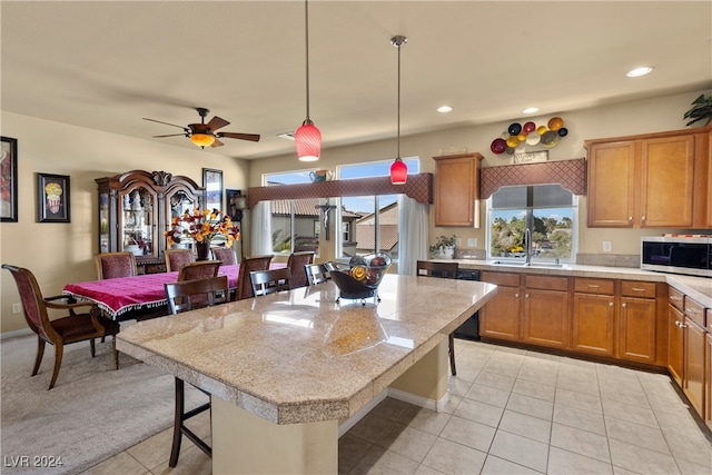 kitchen featuring ceiling fan, light tile patterned floors, a kitchen island, decorative light fixtures, and a breakfast bar area