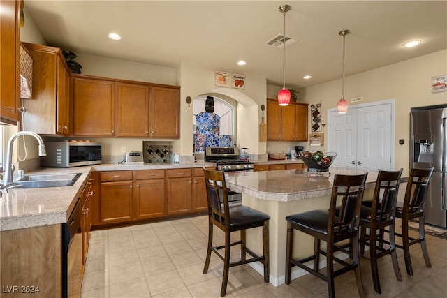 kitchen with a breakfast bar, a center island, sink, hanging light fixtures, and appliances with stainless steel finishes