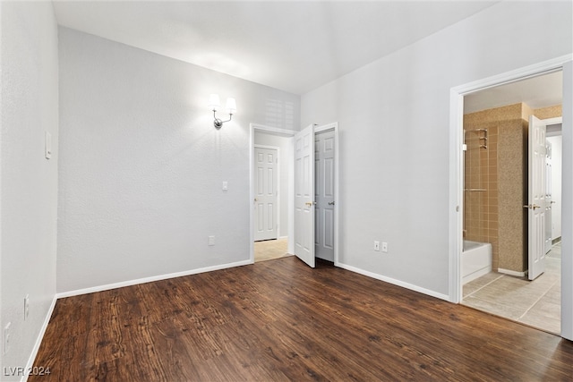 unfurnished bedroom with ensuite bathroom and hardwood / wood-style floors