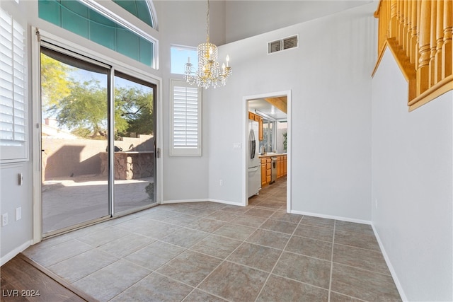 unfurnished dining area with tile patterned flooring, a towering ceiling, and a chandelier