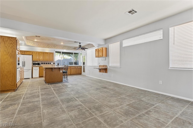 kitchen featuring a breakfast bar, a raised ceiling, white appliances, a kitchen island, and ceiling fan