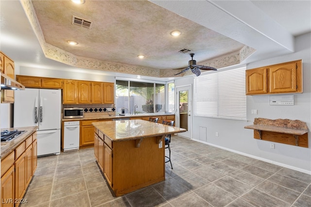 kitchen with a center island, a kitchen bar, stainless steel appliances, a raised ceiling, and ceiling fan