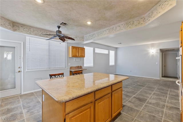 kitchen with light stone counters, ceiling fan, and a kitchen island