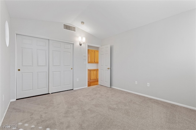 unfurnished bedroom with light carpet, lofted ceiling, and a closet