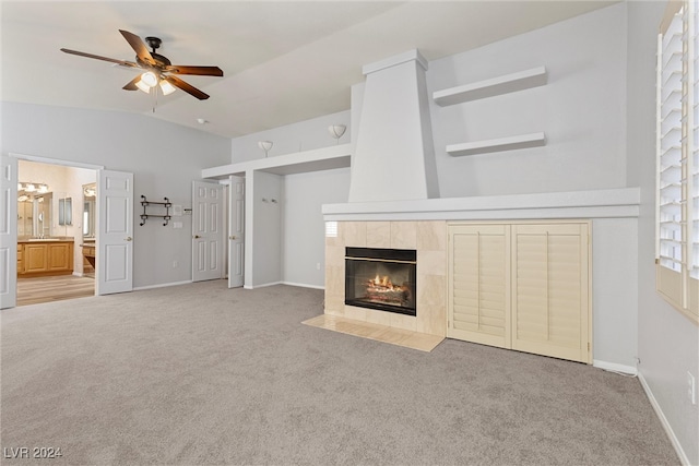 unfurnished living room featuring a tiled fireplace, ceiling fan, vaulted ceiling, and light colored carpet