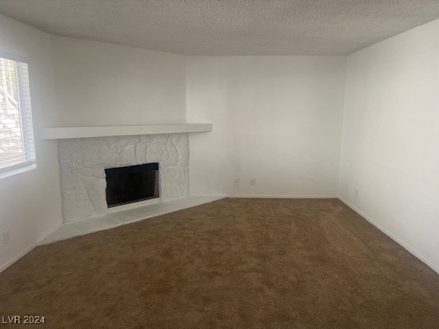 unfurnished living room featuring a stone fireplace, a textured ceiling, and carpet floors