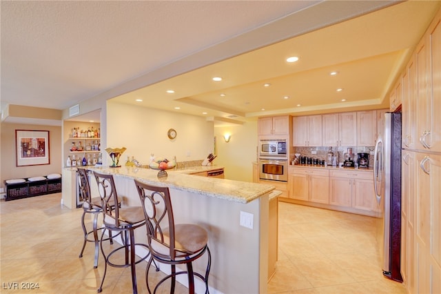 kitchen featuring kitchen peninsula, a breakfast bar area, light stone countertops, stainless steel appliances, and a tray ceiling