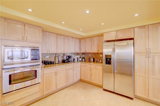 kitchen featuring light brown cabinets, light tile patterned floors, stainless steel appliances, light stone countertops, and decorative backsplash