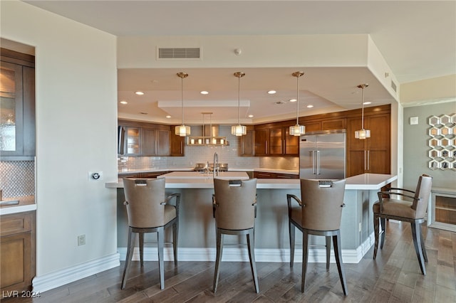 kitchen with stainless steel built in refrigerator, decorative light fixtures, dark wood-type flooring, and a kitchen breakfast bar