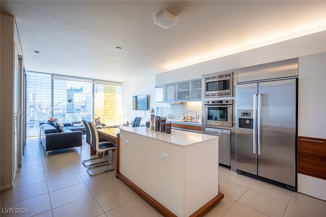 kitchen with white cabinetry, a breakfast bar, a kitchen island, built in appliances, and light tile patterned floors