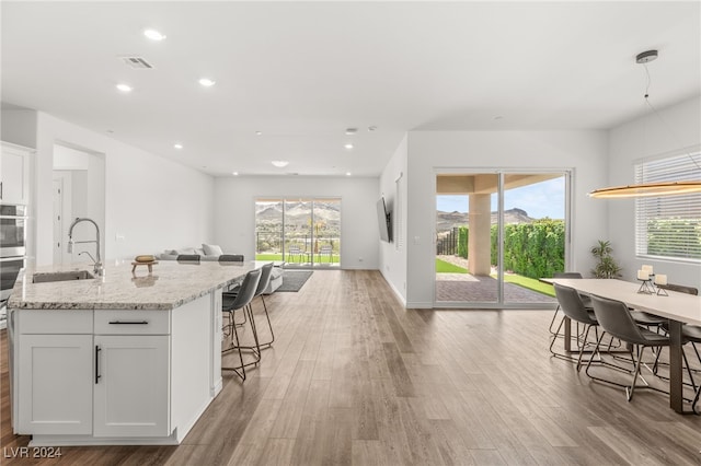 kitchen featuring light stone counters, sink, light hardwood / wood-style flooring, white cabinetry, and a kitchen breakfast bar