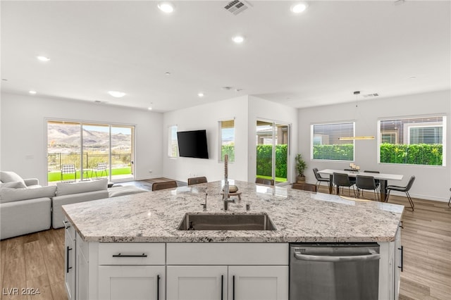 kitchen featuring light wood-type flooring, sink, white cabinetry, a center island with sink, and stainless steel dishwasher