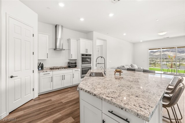 kitchen featuring white cabinets, sink, wall chimney range hood, a kitchen breakfast bar, and hardwood / wood-style floors