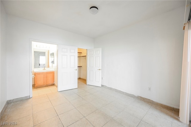 unfurnished bedroom with light tile patterned flooring, ensuite bath, and sink