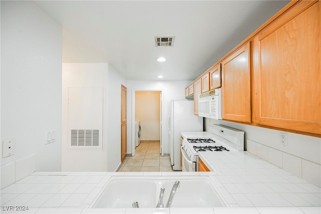 kitchen with white appliances, light tile patterned floors, tile countertops, washer / dryer, and sink