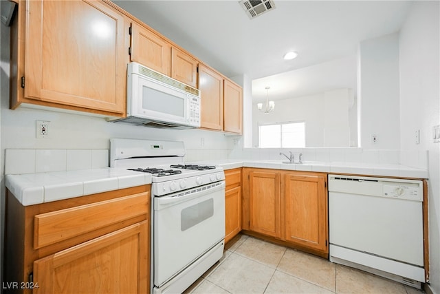 kitchen featuring light tile patterned flooring, white appliances, tile countertops, an inviting chandelier, and sink