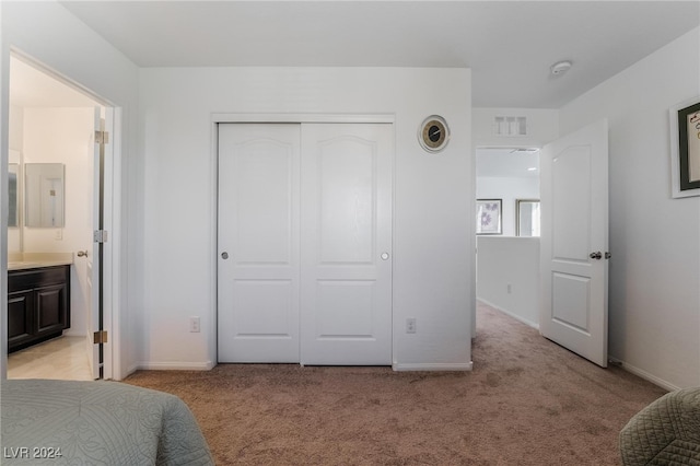 bedroom with light carpet, a closet, and ensuite bathroom