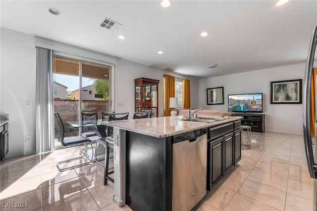 kitchen featuring a breakfast bar, a kitchen island with sink, sink, light stone countertops, and stainless steel dishwasher